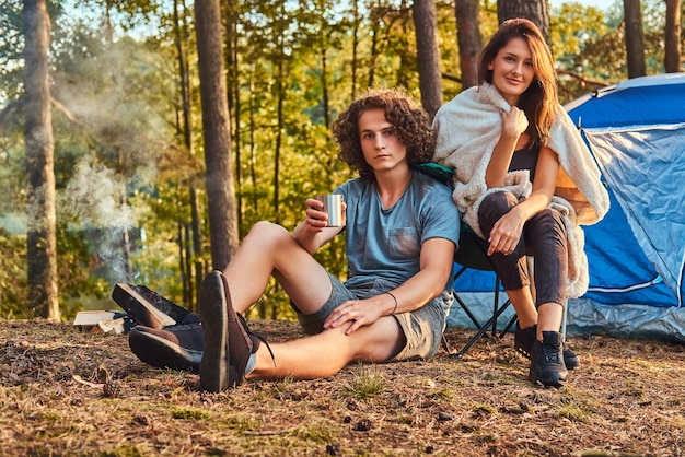 Par de caminatas en el bosque. Atractiva pareja calentándose cerca de una fogata en el campamento. Concepto de viaje, turismo y caminata.