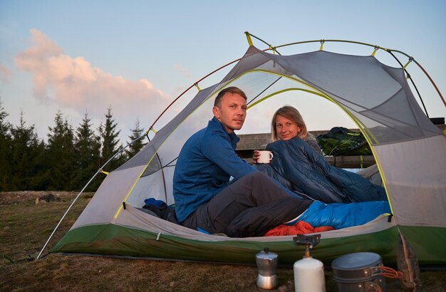 Par de campistas relajándose en carpa al aire libre