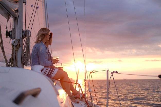 Un par de damas disfrutan de su viaje en velero mientras beben vino y ven una hermosa puesta de sol.