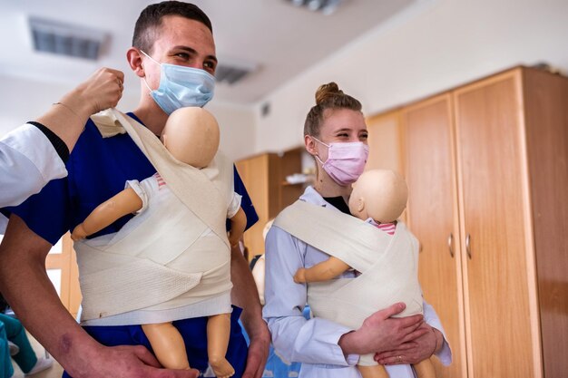 Un par de estudiantes de medicina aprendiendo a sujetar a un bebé y sonriendo mientras reciben ayuda