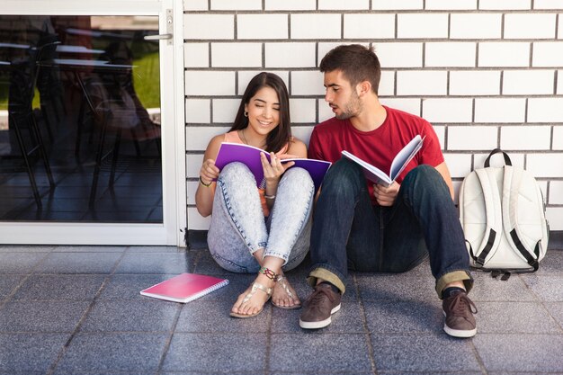 Un par de estudiantes universitarios sentados afuera de un salón de clases y estudiando juntos