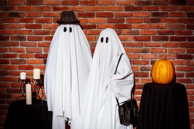 Foto gratuita par de fantasmas posando sobre pared de ladrillo fiesta de halloween.