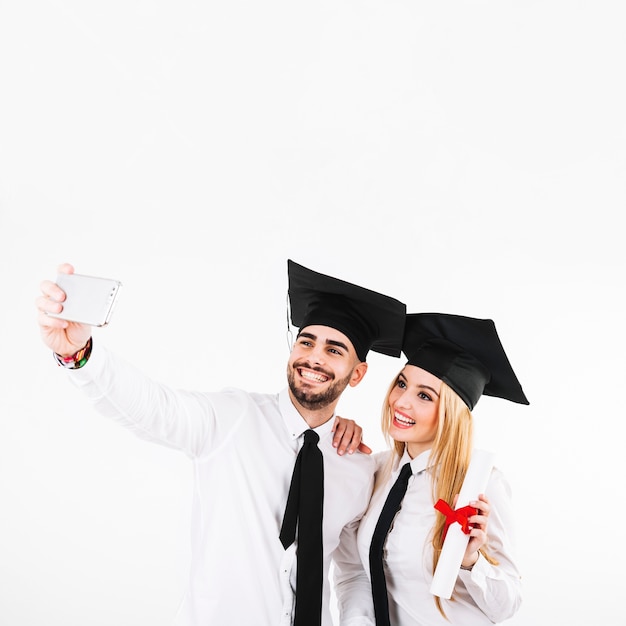 Par de graduación en birretes tomando autofoto