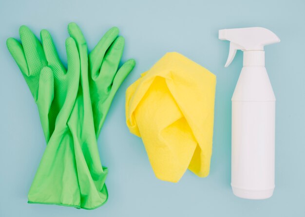 Par de guantes verdes; Servilleta y botella de spray blanco sobre fondo azul