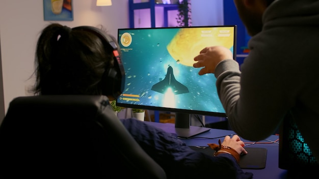 Par de jugadores que juegan al juego multijugador en una computadora potente en casa con auriculares profesionales