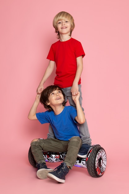 Un par de muchachos de vista frontal con camisetas de colores montando en segway en el espacio rosa