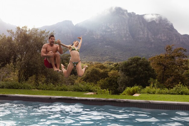 Par saltando juntos en la piscina en el patio trasero