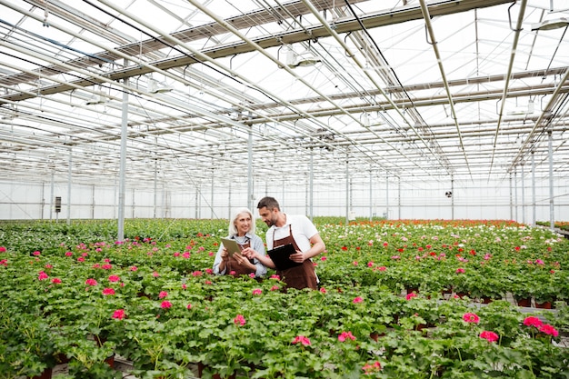 Par de trabajadores de pie en el jardín cerca de flores y hablando