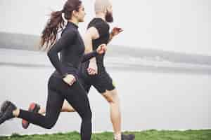 Foto gratuita par trotar y correr al aire libre en el parque cerca del agua. joven barbudo hombre y mujer haciendo ejercicio juntos en la mañana