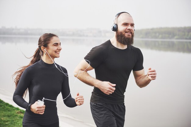 Par trotar y correr al aire libre en el parque cerca del agua. Joven barbudo hombre y mujer haciendo ejercicio juntos en la mañana