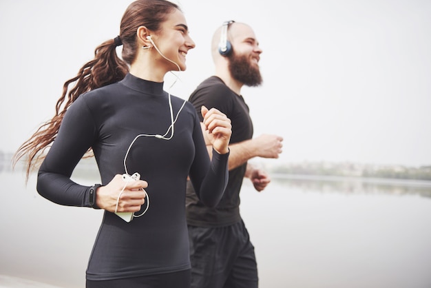 Par trotar y correr al aire libre en el parque cerca del agua. Joven barbudo hombre y mujer haciendo ejercicio juntos en la mañana