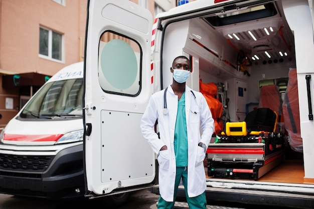 Paramédico masculino africano con máscara médica protectora facial parado frente a un camión de ambulancia