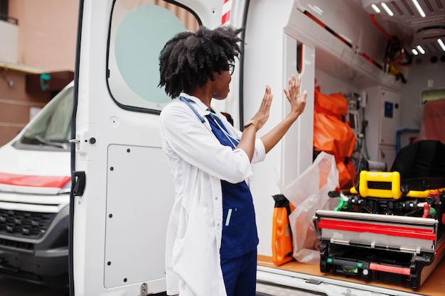 Paramédico mujer afroamericana de pie delante del coche de ambulancia