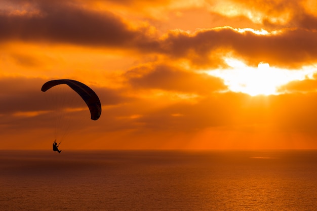 Parapente al atardecer con increíble cielo nublado y sol brillando a través de las nubes