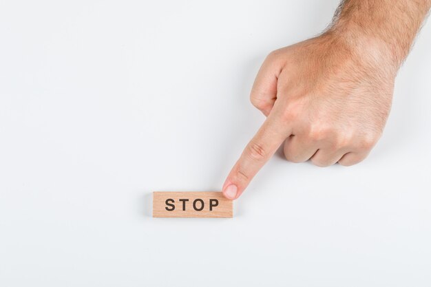 Pare el concepto de la palabra con los bloques de madera en la opinión superior del fondo blanco. con la mano sosteniéndola. imagen horizontal