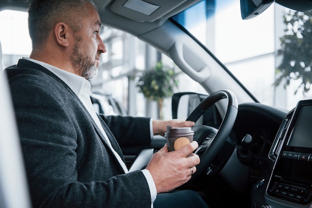 Paré por un descanso. Vista lateral del empresario senior en ropa oficial dentro del automóvil moderno