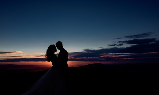 La pareja abraza antes del cielo violeta de la tarde sobre las montañas
