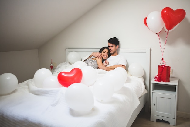 Pareja abrazada en la cama rodeados de globos