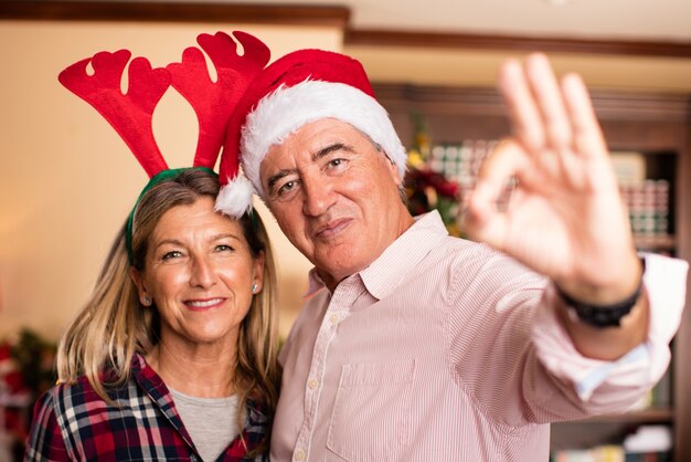 Pareja abrazada con gorros de navidad diciendo okey