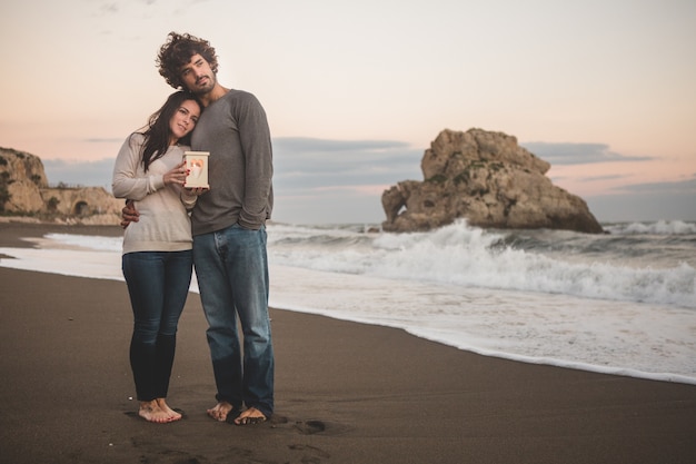 Pareja abrazada en la orilla de la playa sujetando una vela