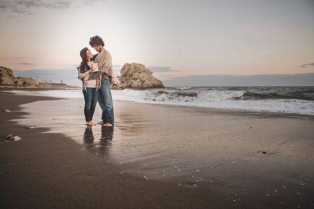 Pareja abrazada en la orilla de la playa sujetando una vela