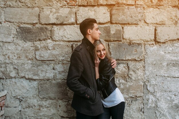 Pareja abrazada con una pared de ladrillos grandes detrás