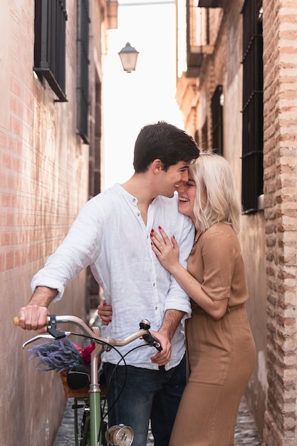 Pareja abrazada posando con bicicleta afuera