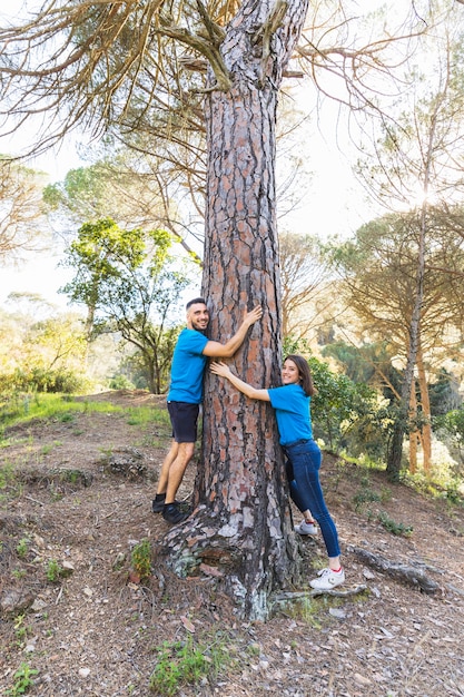 Pareja abrazándose árbol en hermoso bosque