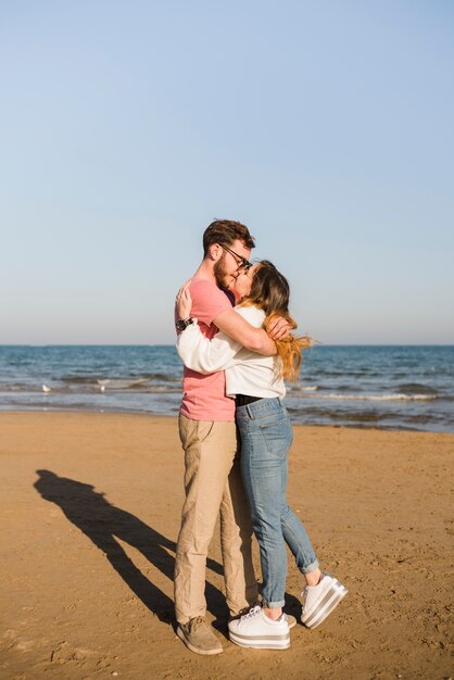 Pareja abrazándose besándose cerca de la orilla del mar en la playa