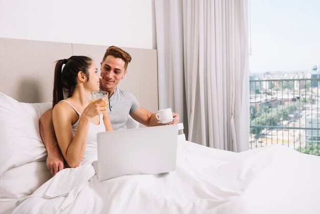 Pareja abrazándose en la cama y desayunando