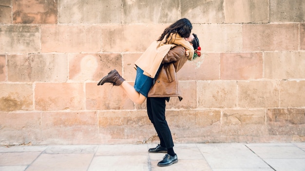 Pareja abrazándose junto a la pared de ladrillo