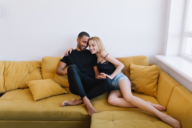 Pareja abrazándose con los ojos cerrados en el sofá. Amantes tomados de la mano, abrazándose. Caras felices, cálida relación, amor, romance.