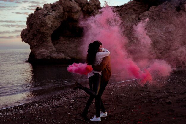 Pareja abrazándose en la orilla del mar con bomba de humo rosa