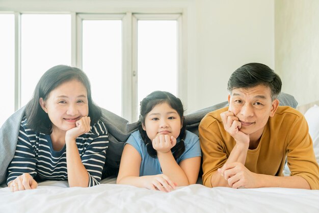 Pareja de abuelos mayores asiáticos acostados con nietos preety niña en la cama en el dormitorio familia feliz jugar juntos en la cama