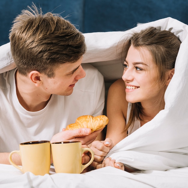 Foto gratuita pareja acostada bajo una manta con café y croissant