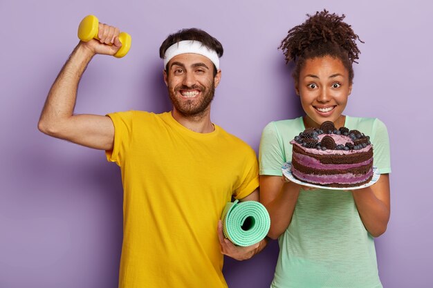 Pareja activa alegre posando con un gran pastel