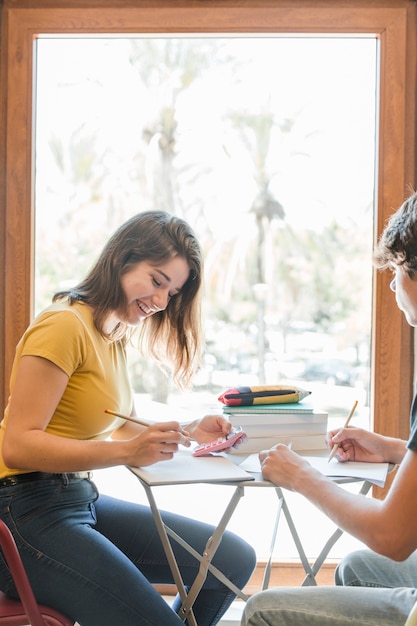 Pareja adolescente haciendo la tarea junto a la ventana