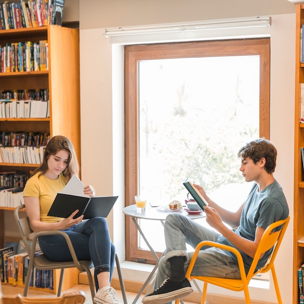 Pareja adolescente leyendo en la biblioteca