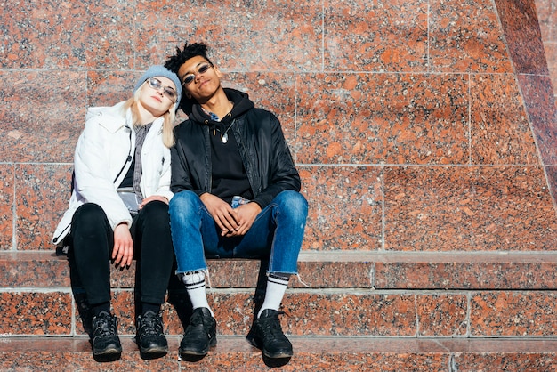 Pareja adolescente de moda sentados juntos al aire libre