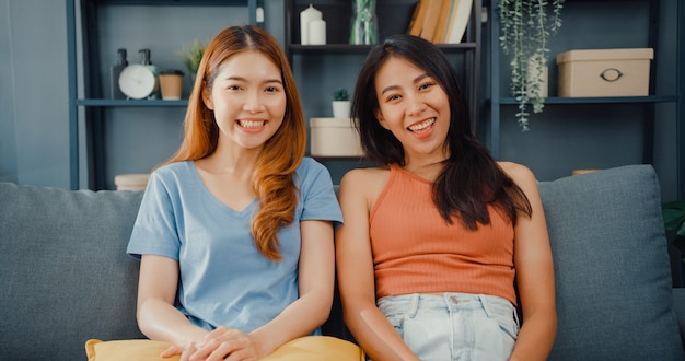 Pareja de adolescentes mujeres asiáticas que se sienten felices sonriendo y mirando al frente mientras se relajan en la sala de estar en casa