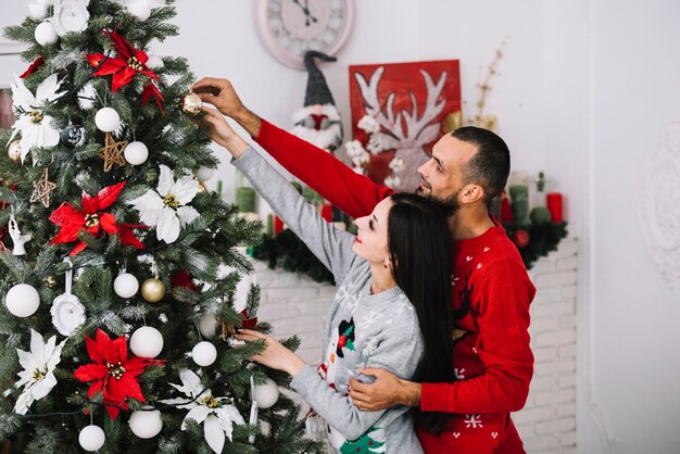 Pareja con adorno de bola cerca del árbol de navidad