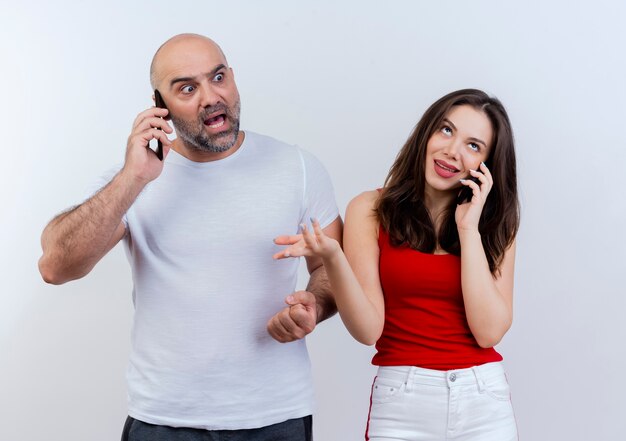 Pareja adulta hablando por teléfono impresionado hombre mirando al lado y mujer despistada mirando hacia arriba