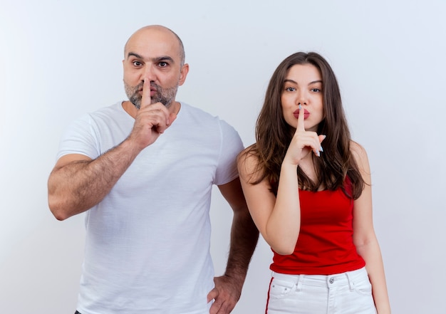 Pareja adulta hombre manteniendo la mano en la cintura mirando y gesticulando silencio