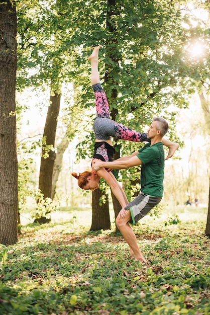 Pareja adulta media sana haciendo ejercicios de yoga acrobático en el parque