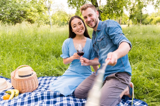 Pareja adulta multirracial sentado tomando selfie con palo