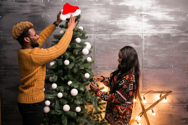 Pareja afroamericana colgando juguetes en un árbol de Navidad