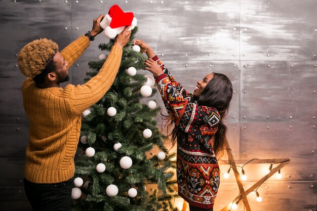 Pareja afroamericana colgando juguetes en un árbol de Navidad