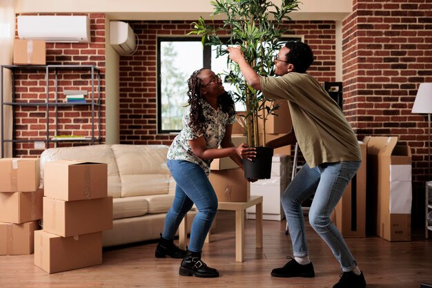 Pareja afroamericana decorando un nuevo apartamento para mudarse, desempacando plantas y muebles en la sala de estar. Reubicar la propiedad del hogar después de comprar la primera casa juntos, evento de vida.