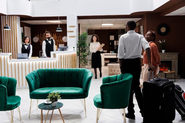 Foto gratuita pareja afroamericana en recepción, llegando al hotel y preparándose para hacer el proceso de registro. hombre y mujer felices preguntando al personal de recepción sobre la reserva de habitaciones, rellenando formularios de registro.