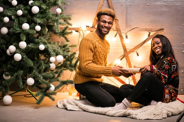 Pareja afroamericana sentada junto al árbol de Navidad